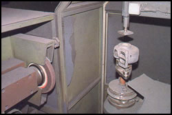 Inside the fettling machine, showing a casting mounted in a fixture and the grinding wheel