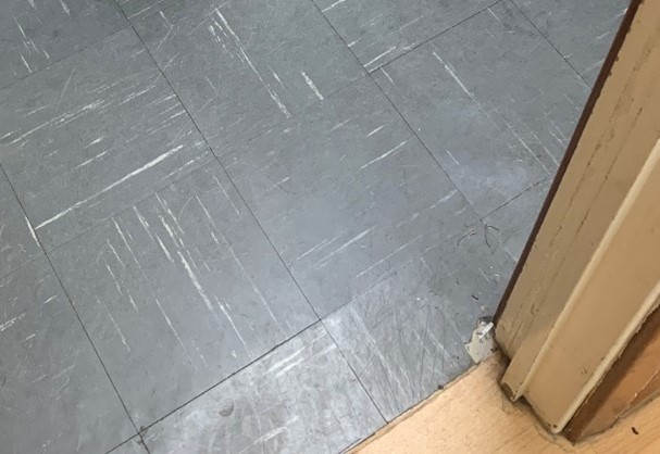 Image of grey and white vinyl floor tiles with one damaged by door frame